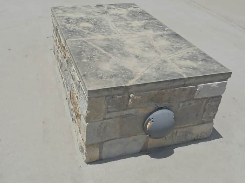 Limestone cap on a stone planter outside an office building, darkened with weathering and organic growth.