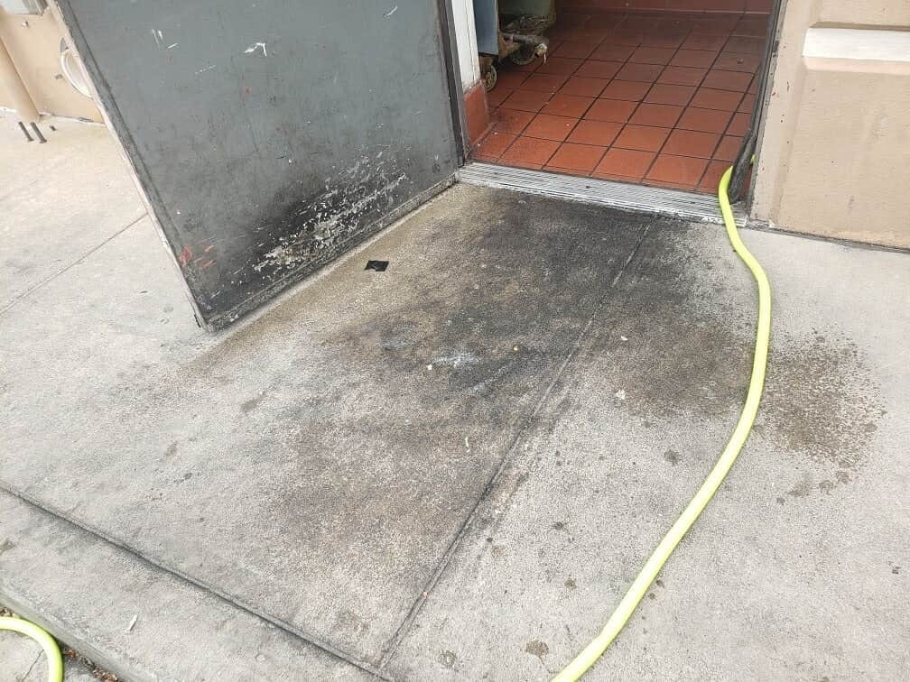 Concrete outside a restaurant kitchen exit, stained black with built-up cooking grease.
